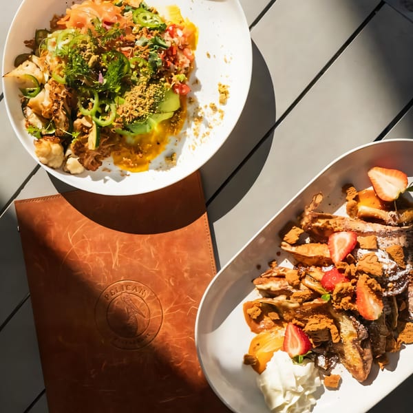 Overhead view of two American dishes, one savory and one sweet, on a gray table with a Pelican Restaurant menu.