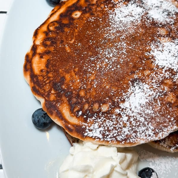 Fluffy pancakes topped with powdered sugar, fresh blueberries, and whipped cream on a white plate.