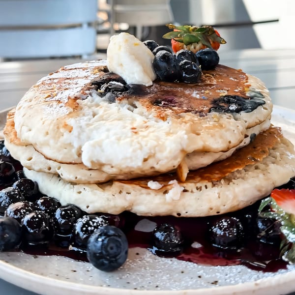 A stack of blueberry pancakes with syrup, powdered sugar, whipped cream, and a strawberry.