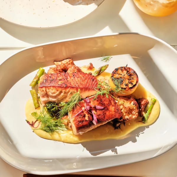 Grilled salmon with asparagus, dill, and a charred lemon on a white plate with yellow sauce.